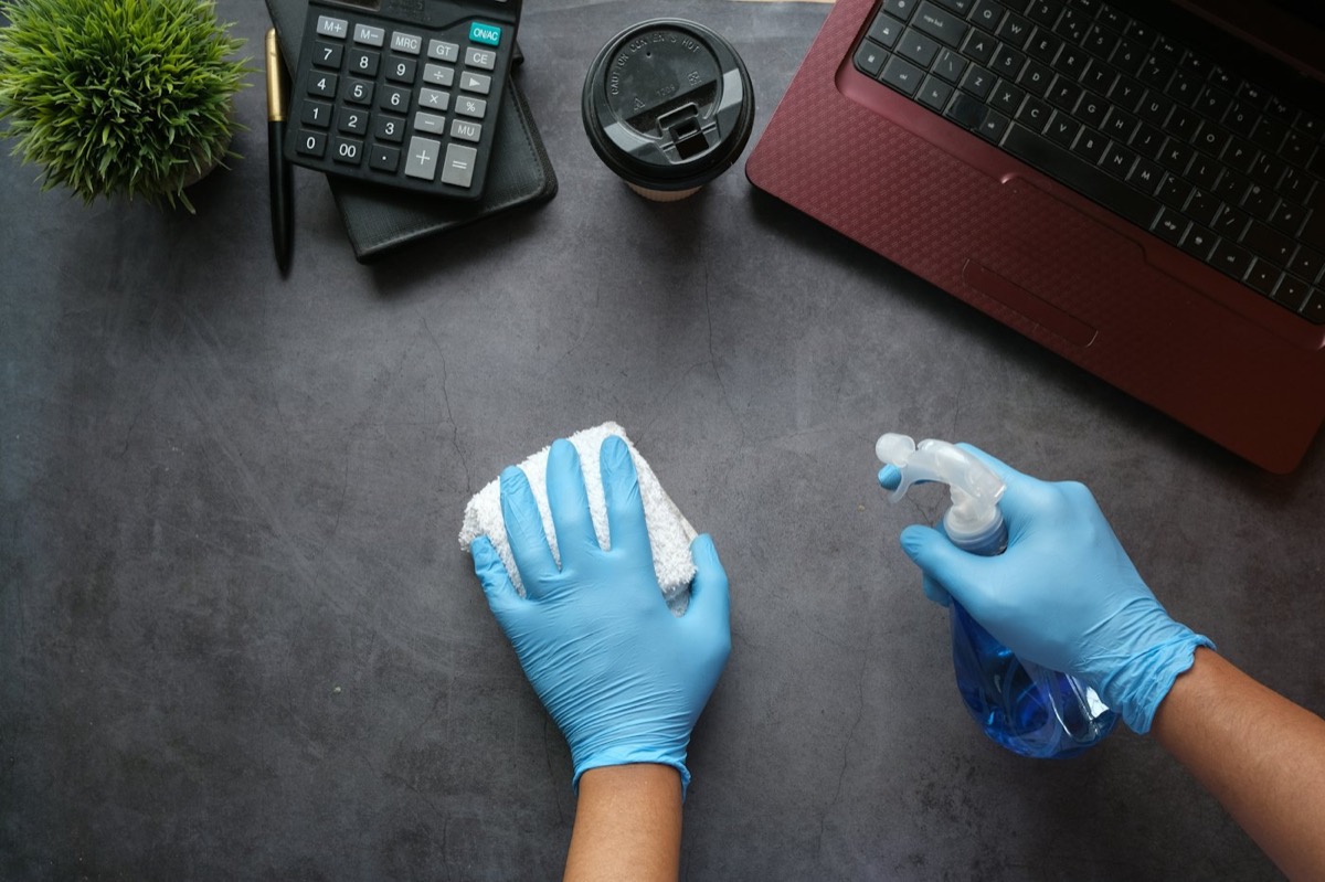 Limpieza de un escritorio de oficina con guantes y pulverizador